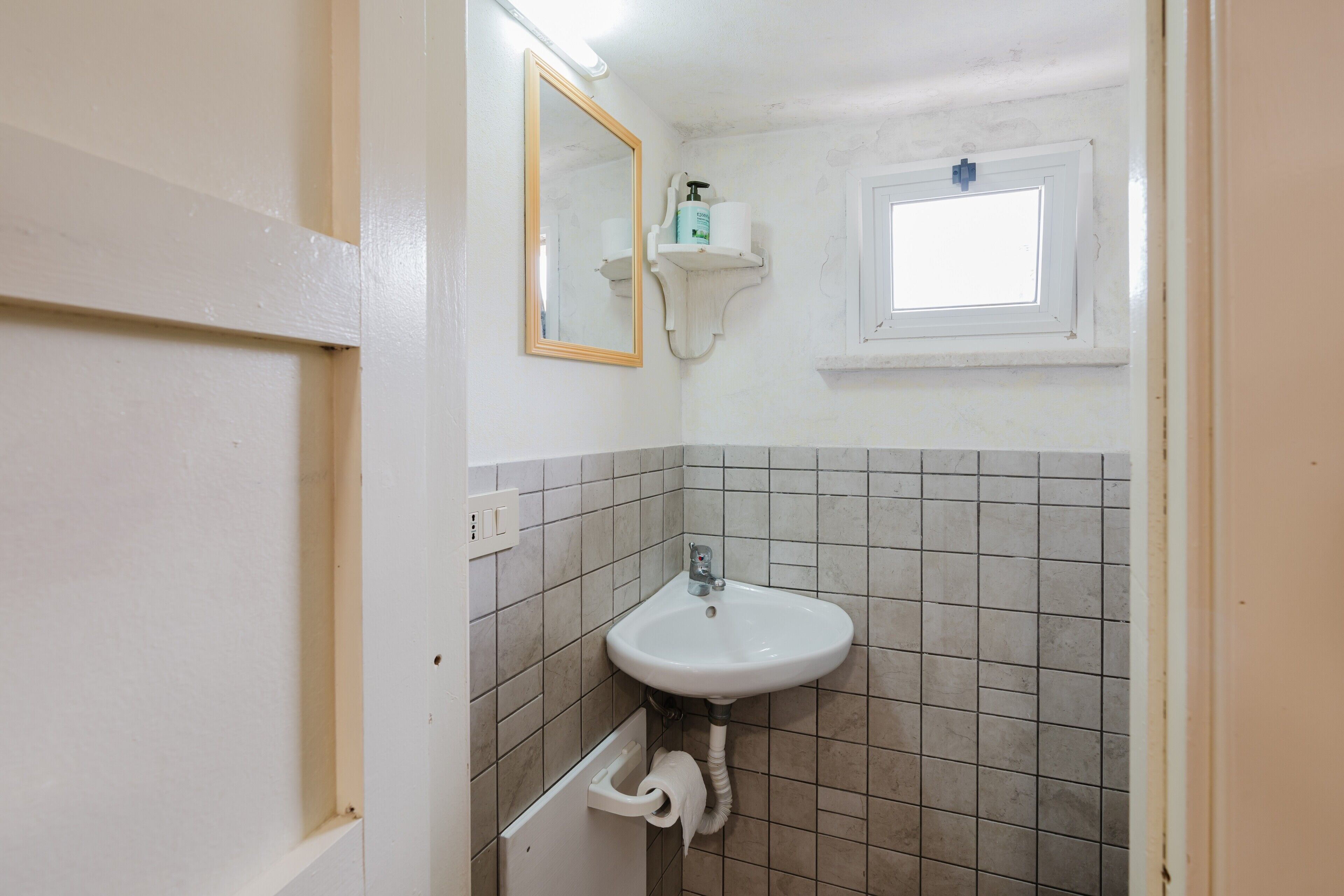 Ein Badezimmer mit Waschbecken, Spiegel, Seifenspender und Fenster.