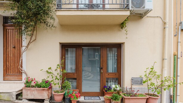 A building with a wooden door, potted plants, and a balcony with an air conditioning unit.