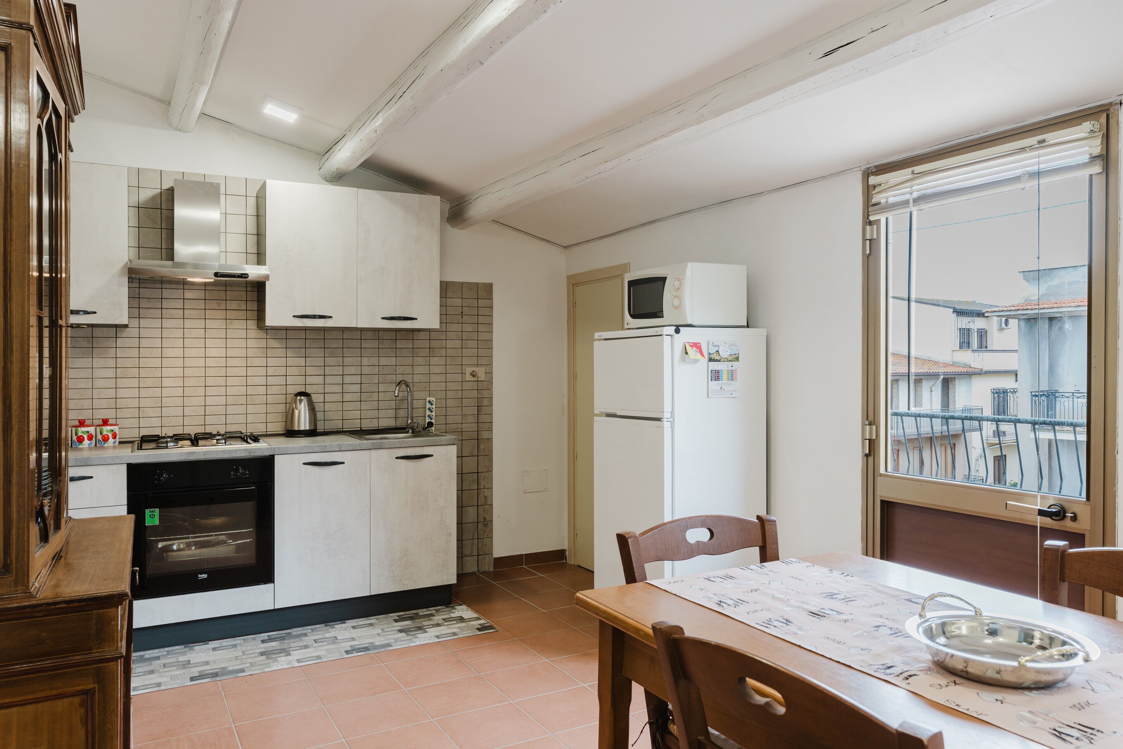 A kitchen with white cabinets, a microwave, a refrigerator, and a dining table with chairs.