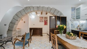 Un comedor con un arco de piedra, mobiliario de madera, piso de baldosas y una cocina con armarios blancos.