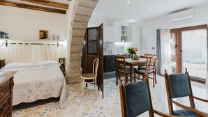 Un dormitorio con cama, una silla de madera, una mesa de comedor con sillas, una zona de cocina y un balcón con vistas.
