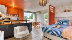 A modern bedroom with a bed, a chair, a dining area, and a kitchen. - Apartment "Sunny Day" with Private Terrace and Air Conditioning (La Grande-Motte)