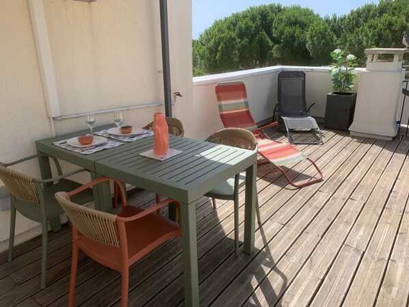 Una terraza de madera con una mesa y sillas, una planta en maceta y un pájaro en un alféizar.