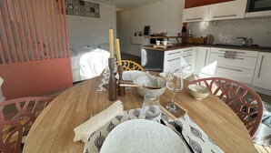A dining area with a round table set for four, a kitchen with white cabinets, and a staircase with orange railings. - Apartment "Sunny Day" with Private Terrace and Air Conditioning (La Grande-Motte)