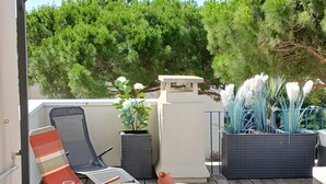 A wooden deck with a table and chairs, a striped chair, and a potted plant. - Apartment "Sunny Day" with Private Terrace and Air Conditioning (La Grande-Motte)