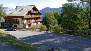 A mountain lodge with a parking area, wooden balconies, and a view of the surrounding forest and mountains.
