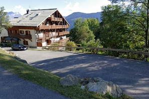 Un chalet de montagne doté d’un espace de stationnement, de balcons en bois et offrant une vue sur la forêt et les montagnes environnantes.