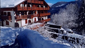 A chalet-style building with multiple balconies, surrounded by snow-covered trees and mountains.