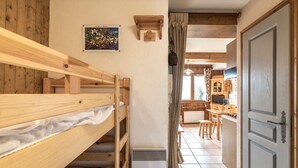 A wooden bunk bed with a small picture frame, a kitchen area with wooden cabinets, and a door.