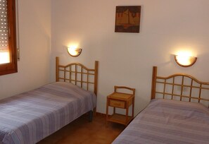 Une chambre avec deux lits simples, une petite chaise en bois et des lampes fixées au mur.