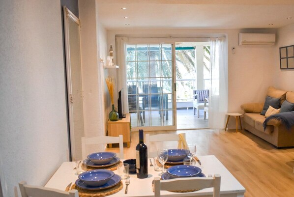 Un comedor con una mesa dispuesta para cuatro, un sofá y vistas a un espacio exterior a través de una puerta de vidrio.