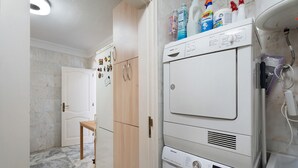 Ett tvättrum med en tvättmaskin och torktumlare placerade ovanpå varandra, träskåp, en vit dörr och ett golv belagt med marmorplattor.