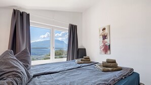 A bedroom with a large window, a bed with grey bedding, a painting on the wall, and a speaker. - Villa 'Renè' with Private Terrace, Wi-Fi and Air Conditioning (Tenno)