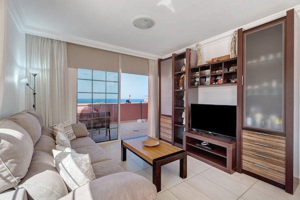 A living room with a sofa, a coffee table, a TV, and a bookshelf.