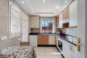 A kitchen with a window, wooden cabinets, a black countertop, and a dining table with a patterned tablecloth.
