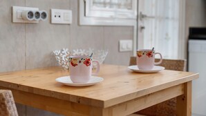 Une table en bois sur laquelle reposent deux tasses ornées de motifs floraux, accompagnées de leurs soucoupes, un élément décoratif blanc accroché au mur et, au fond, une porte blanche.