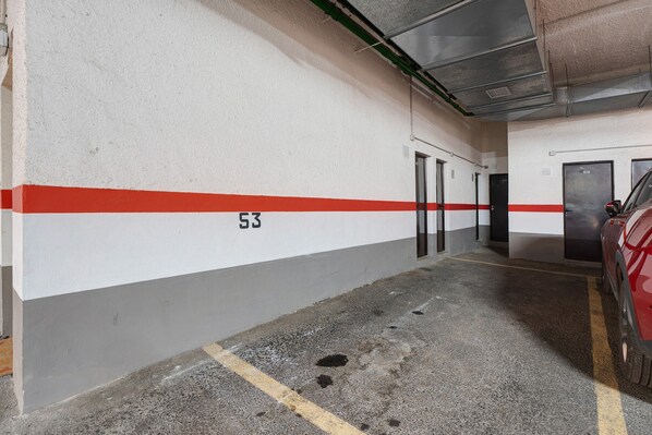 Un aparcamiento con pared blanca, una franja roja y el número 53.