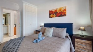 Une chambre à coucher avec un lit, une table de chevet, une lampe, un tableau et une armoire.