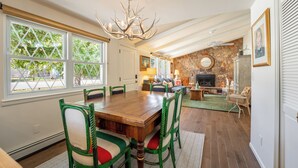 A dining area with a wooden table and green upholstered chairs, a chandelier, and a stone fireplace in the background.