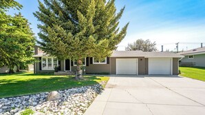 A residential house with a garage, a well-maintained lawn, and a large tree in front.