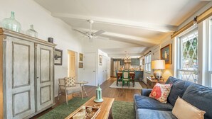 A spacious living room with a blue sofa, a wooden coffee table, and a green rug. There is a dining area with a table and chairs in the background.