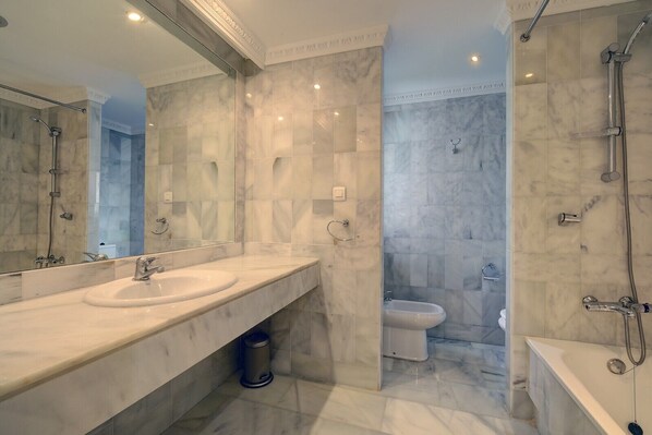 Un baño con paredes de mármol, lavamanos doble, ducha con cerramiento de vidrio y bañera.