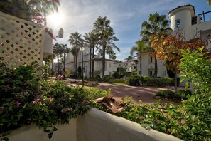 Una zona residencial con palmeras, un edificio blanco de techo curvo y una valla de celosía.