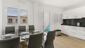 Une cuisine moderne avec des meubles blancs, un plan de travail noir et une table à manger en verre pour quatre personnes.