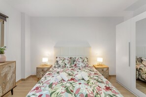 Un dormitorio con edredón estampado con flores, mesitas de noche de madera, un armario y un espejo.