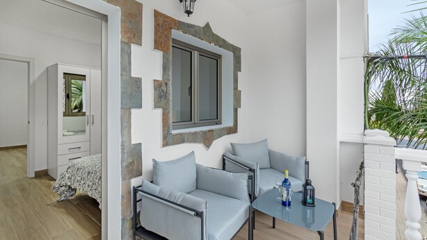 Un salon moderne avec un canapé, une table en verre et une fenêtre donnant sur un mur d’accent en pierre.
