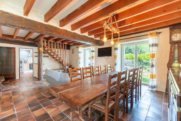 Un área de comedor con una mesa y sillas de madera, una escalera, un televisor y un reloj.