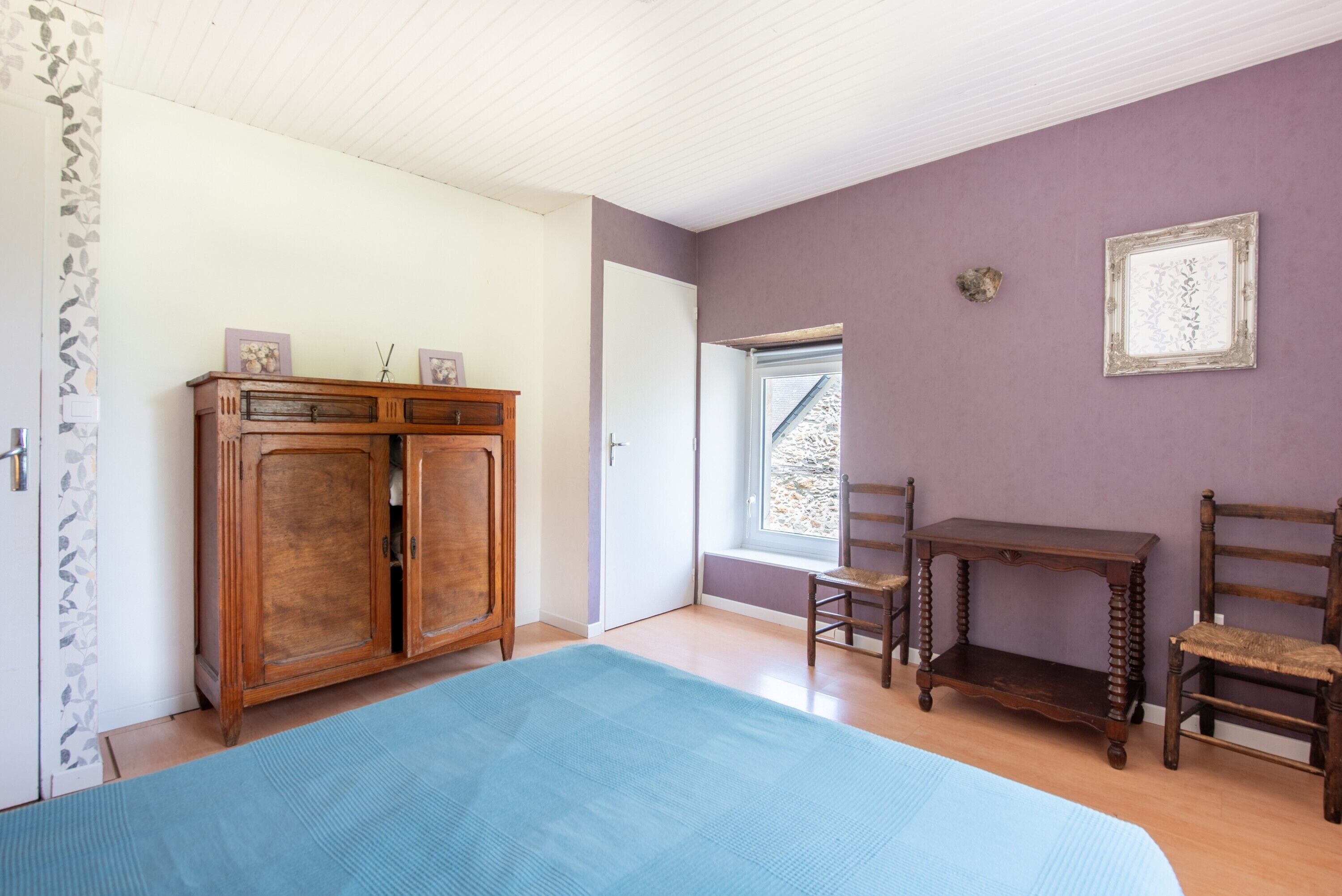 Une chambre avec un grand lit, une armoire en bois, une petite table et une fenêtre donnant sur un beau paysage.