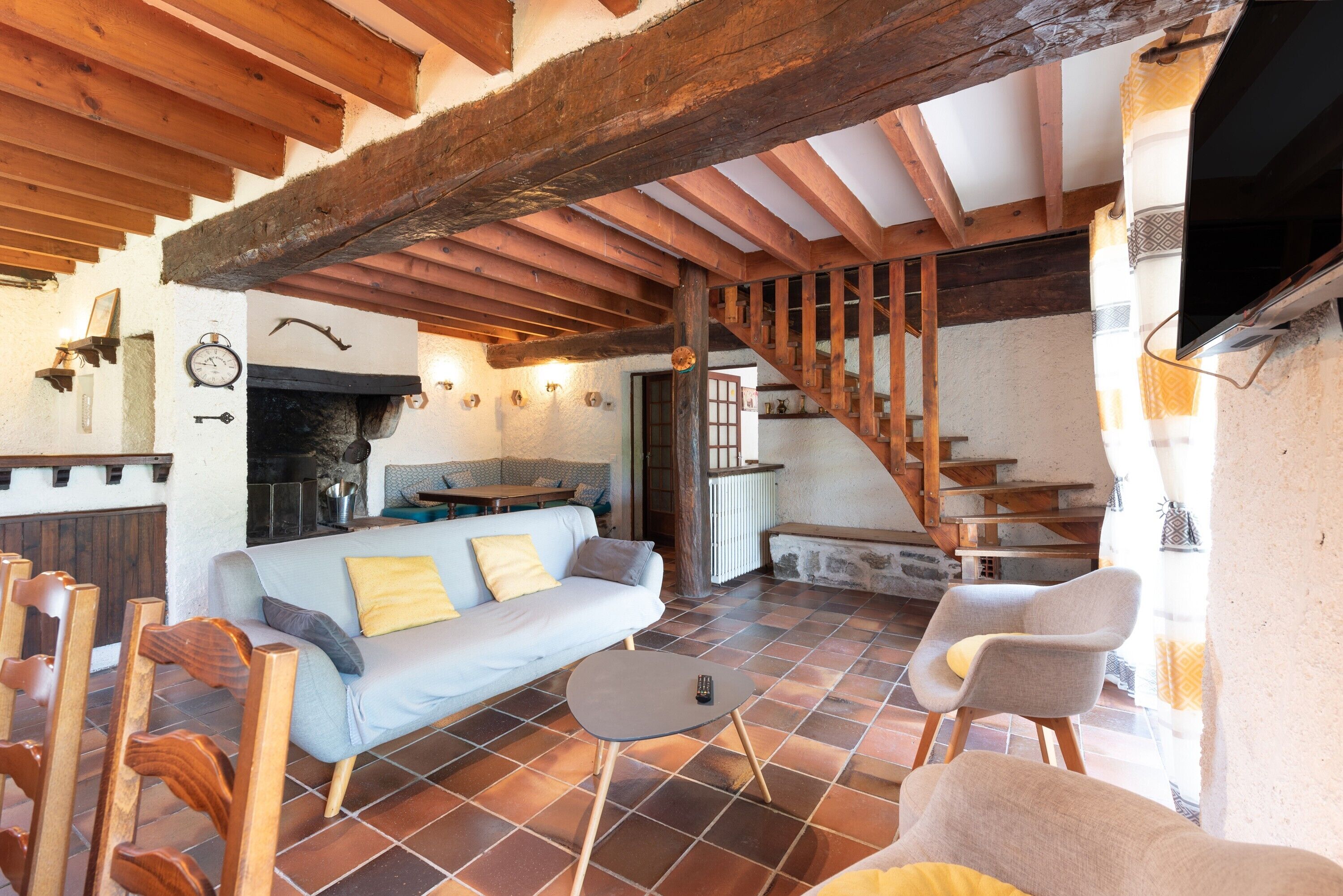 A rustic interior with exposed wooden beams, a stone fireplace, a sofa, and a staircase.