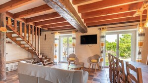 Ein rustikaler Innenraum mit einer Holztreppe, einer Couch, Stühlen, einem Esstisch und einem Fernseher.