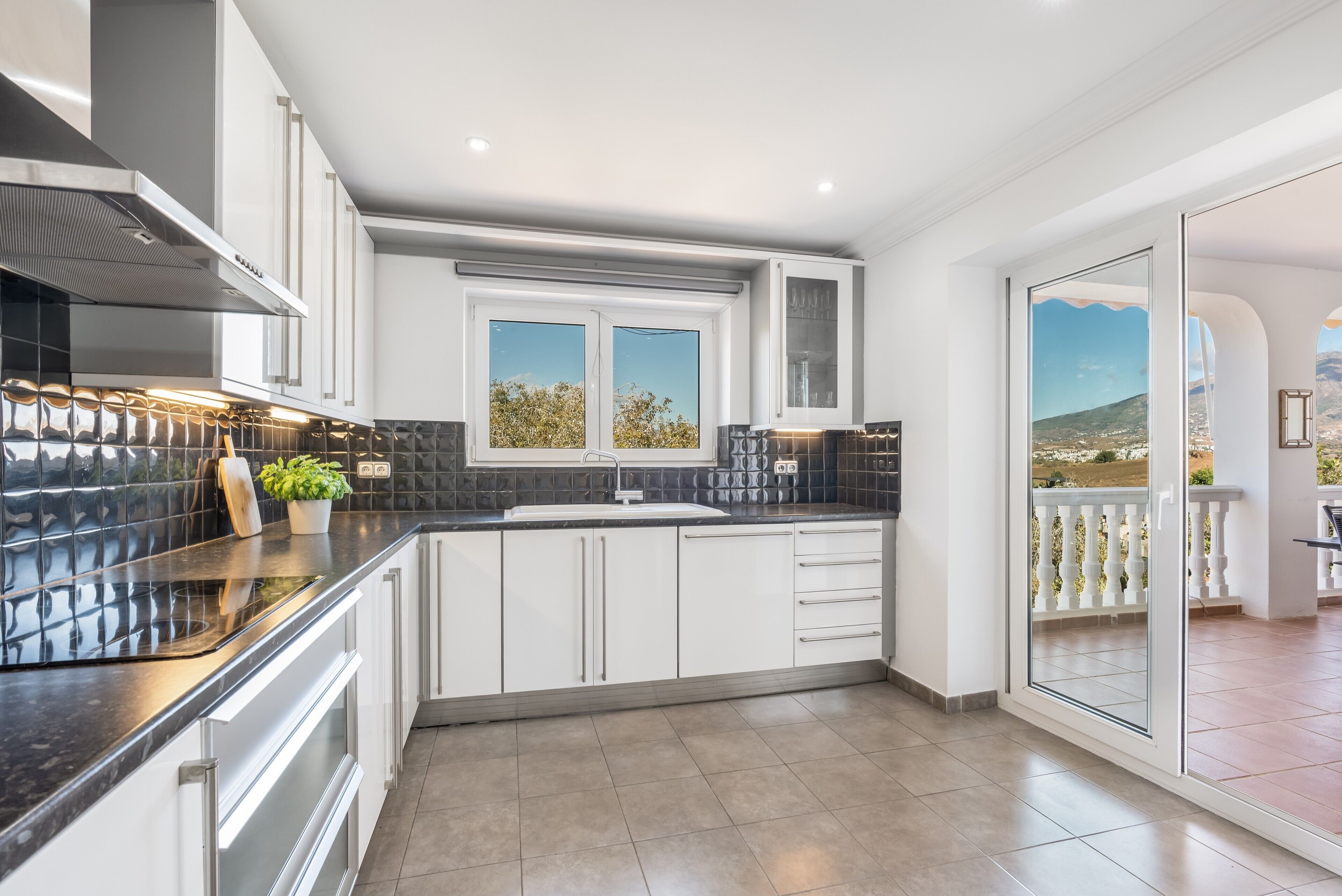 A modern kitchen with a large window, white cabinets, and a black countertop.