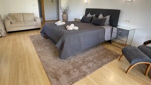 Un dormitorio moderno con cama, sofá, banqueta y un florero con ramas.