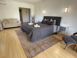 Un dormitorio moderno con cama, sofá, banqueta y un florero con ramas.