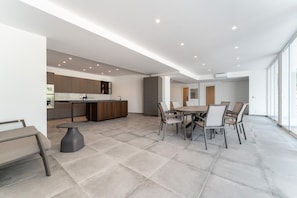 A modern kitchen with a dining area, large windows, and a neutral color palette.