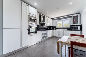 A modern kitchen with white cabinets, stainless steel appliances, and a dining area with a table and chairs. - Holiday Home 'Milano' with Mountain View, Wi-Fi and Air Conditioning (Las Lagunas de Mijas)