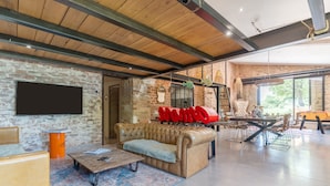 A spacious living area with a leather sofa, a coffee table, and a television mounted on a brick wall. - Apartment 'La Bergerie' with Shared Pool, Wi-Fi and Air Conditioning (Esparron)