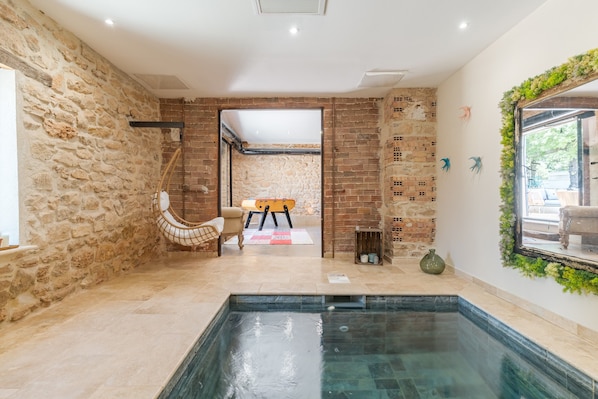 A modern interior with a stone wall, a pool, a wooden bench, and a mirror with greenery.