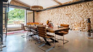 A dining area with a stone wall, a large table, and chairs. - Apartment 'La Bergerie' with Shared Pool, Wi-Fi and Air Conditioning (Esparron)
