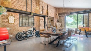 A dining area with a brick wall, a motorcycle, and a table with chairs. - Apartment 'La Bergerie' with Shared Pool, Wi-Fi and Air Conditioning (Esparron)
