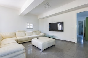 A modern living room with a sectional sofa, a glass coffee table, and a flat-screen TV mounted on the wall.