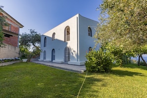 A building with arched windows and a flat roof, surrounded by a well-maintained lawn and a tree.
