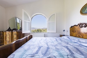 A bedroom with a bed, a dresser, a mirror, and a window with an open shutter.