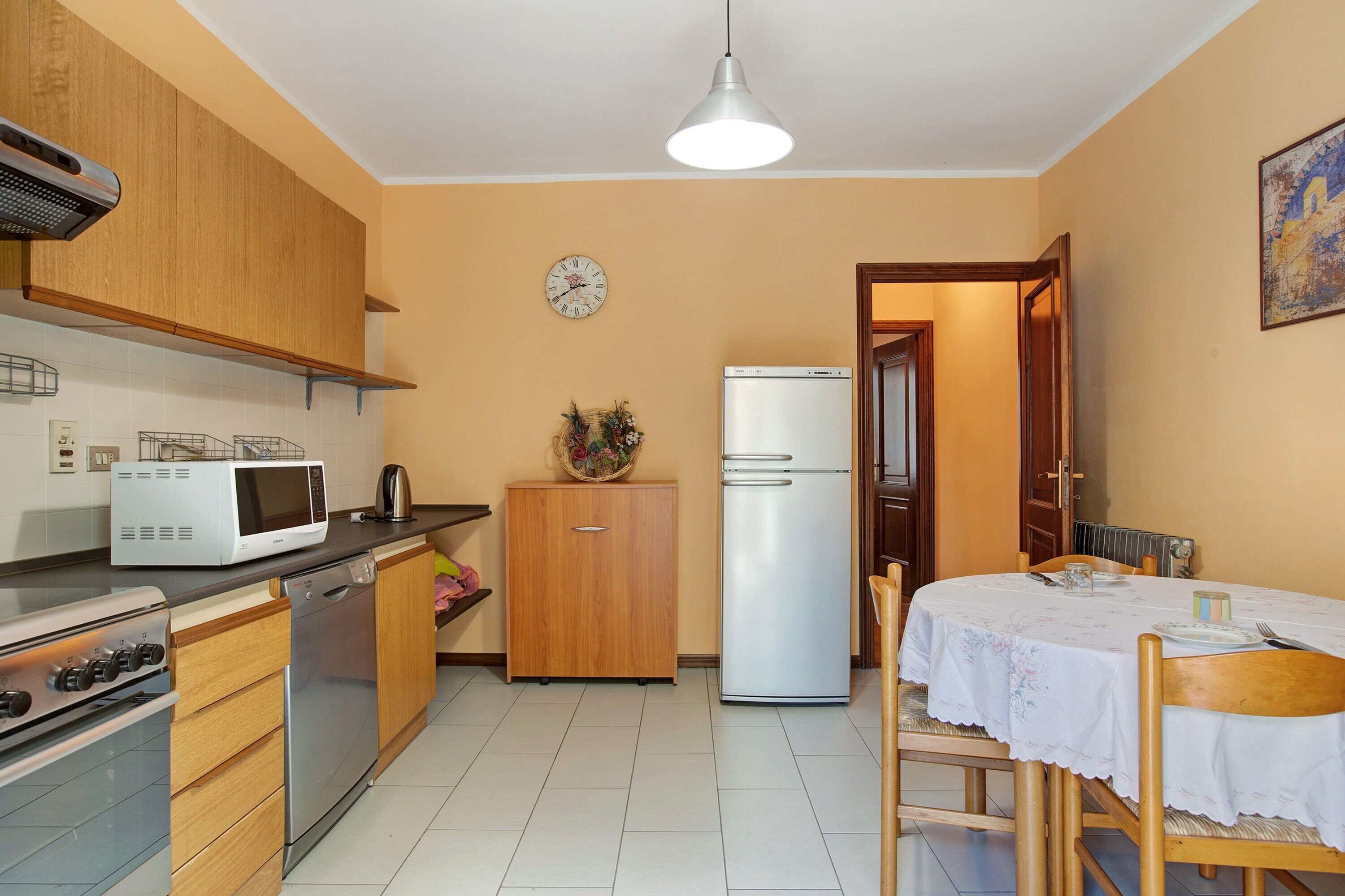 A compact kitchen with a microwave, stove, refrigerator, wooden cabinets, and a dining area with a table and chairs.