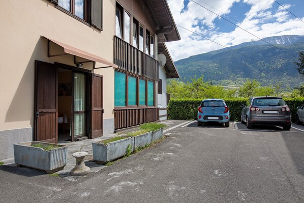 A building with a balcony, a carport with two cars, and a mountainous landscape in the background.