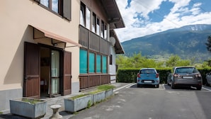 Un edificio con balcón, un porche cubierto con dos coches, y vistas a montañas.