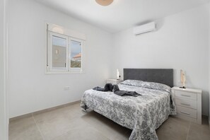 Un dormitorio con cama, mesitas de noche, ventana y aire acondicionado.